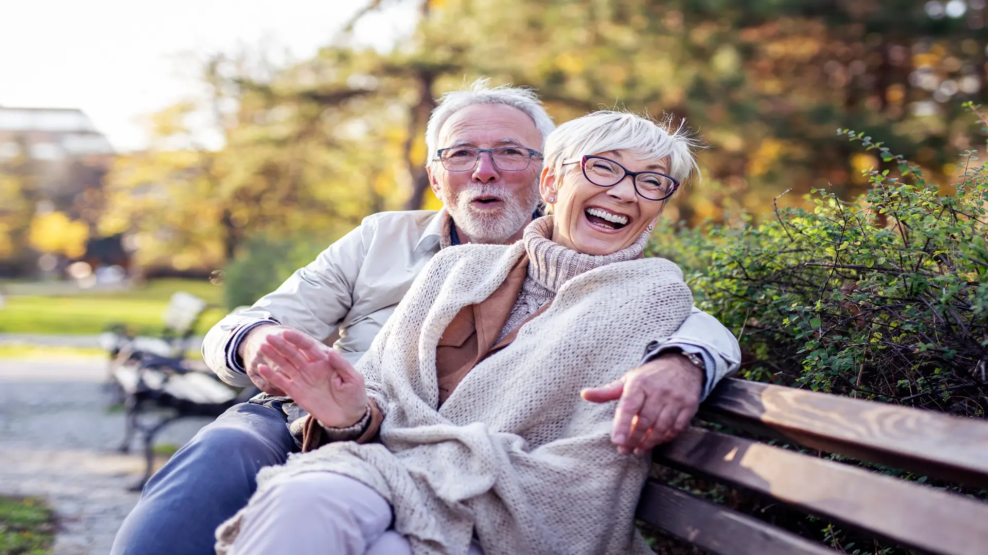 Mature couple sitting on a bench in a public park, talking and smiling